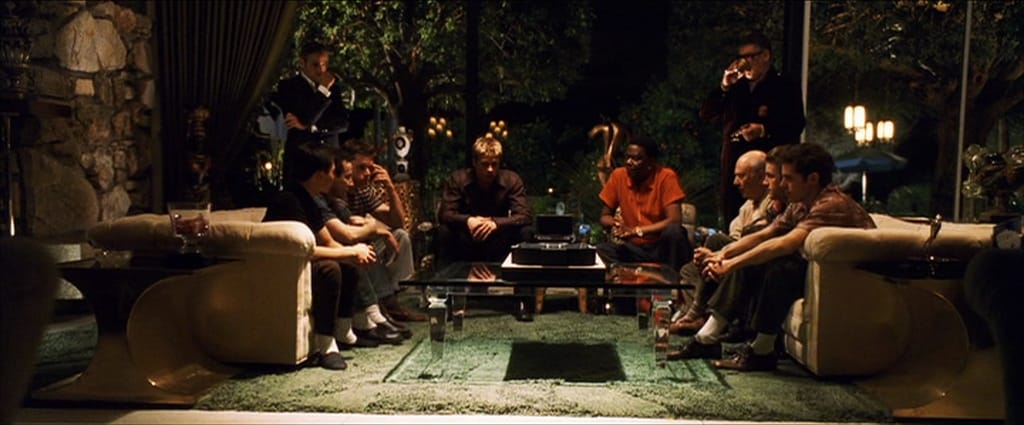 A group of men all sit on couches around a table
