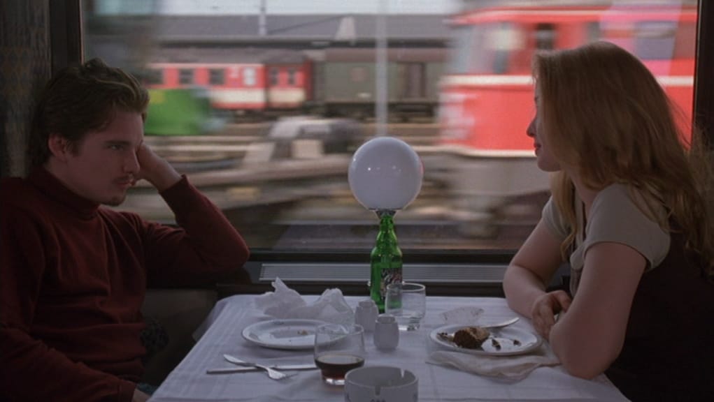 A man and woman in a train sit at a table across from each other.